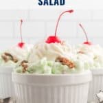 Three white ramekins filled with green Watergate salad, topped with whipped cream, a cherry, and pecans.