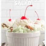 A white ramekin of green Watergate salad topped with whipped cream, a cherry, and walnuts, with a spoon nearby.