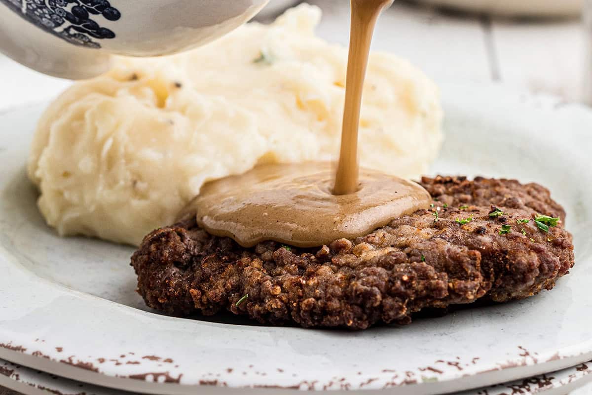 Country fried steak on a plate with gravy being poured on top.