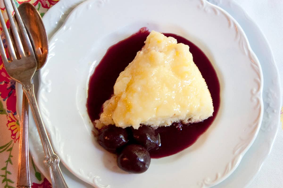 A serving of lemon pudding cake with cherry coulis on a white plate.