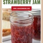 A jar of homemade strawberry jam with bread slices and another jar in the background.