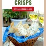 A basket of asiago cheese crisps on a blue napkin, with two glasses of white wine in the background.