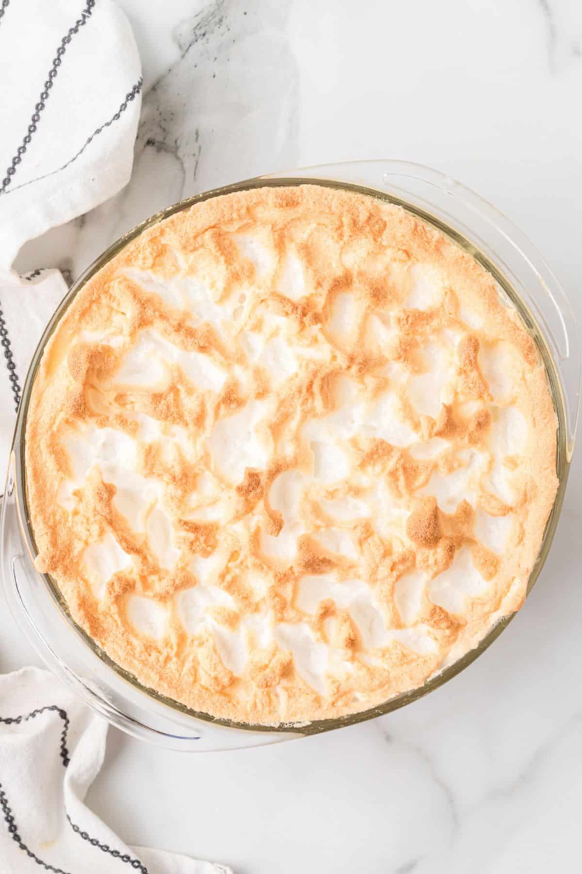 A glass pie dish filled with golden-browned meringue topping on a marble surface.