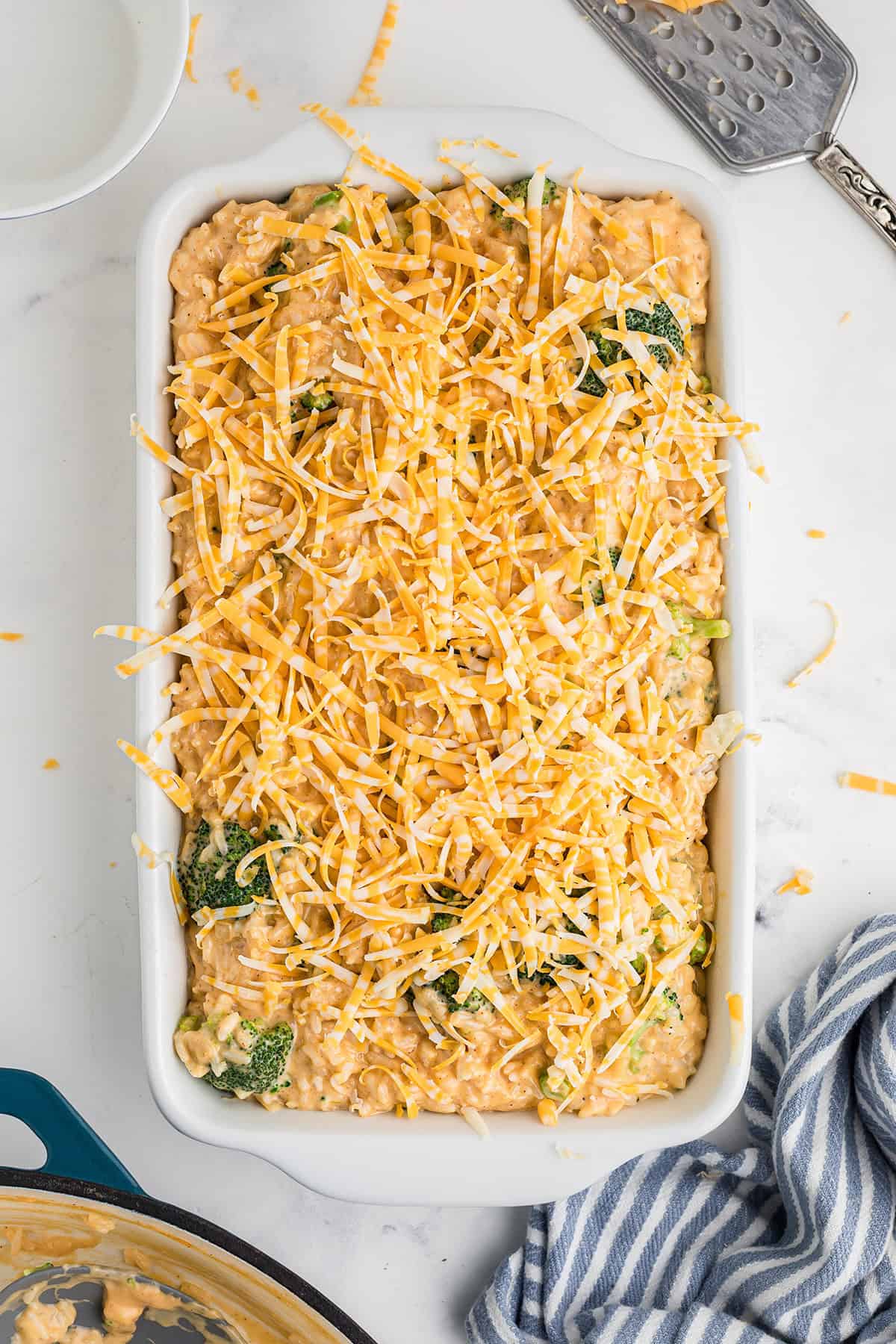 Unbaked casserole topped with shredded cheese in a white dish on a white countertop.