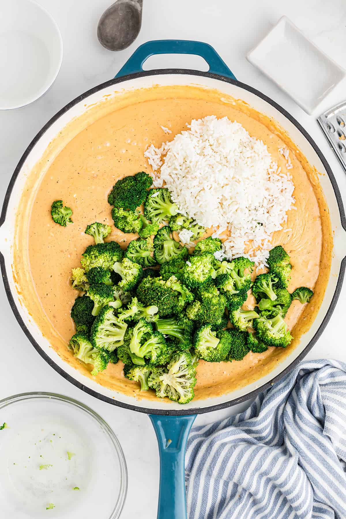 A skillet with orange sauce, cooked broccoli, and a mound of white rice, ready to be mixed.