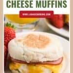 English muffin sandwich with ham, egg, and melted cheese on a plate, with strawberries and juice in the background.