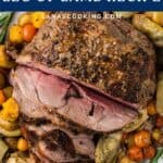 Sliced roasted boneless leg of lamb on a platter with potatoes, tomatoes, and artichokes.