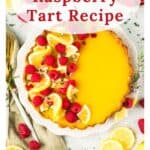 Lemon raspberry tart garnished with raspberries and lemon slices, displayed on a white table with utensils.