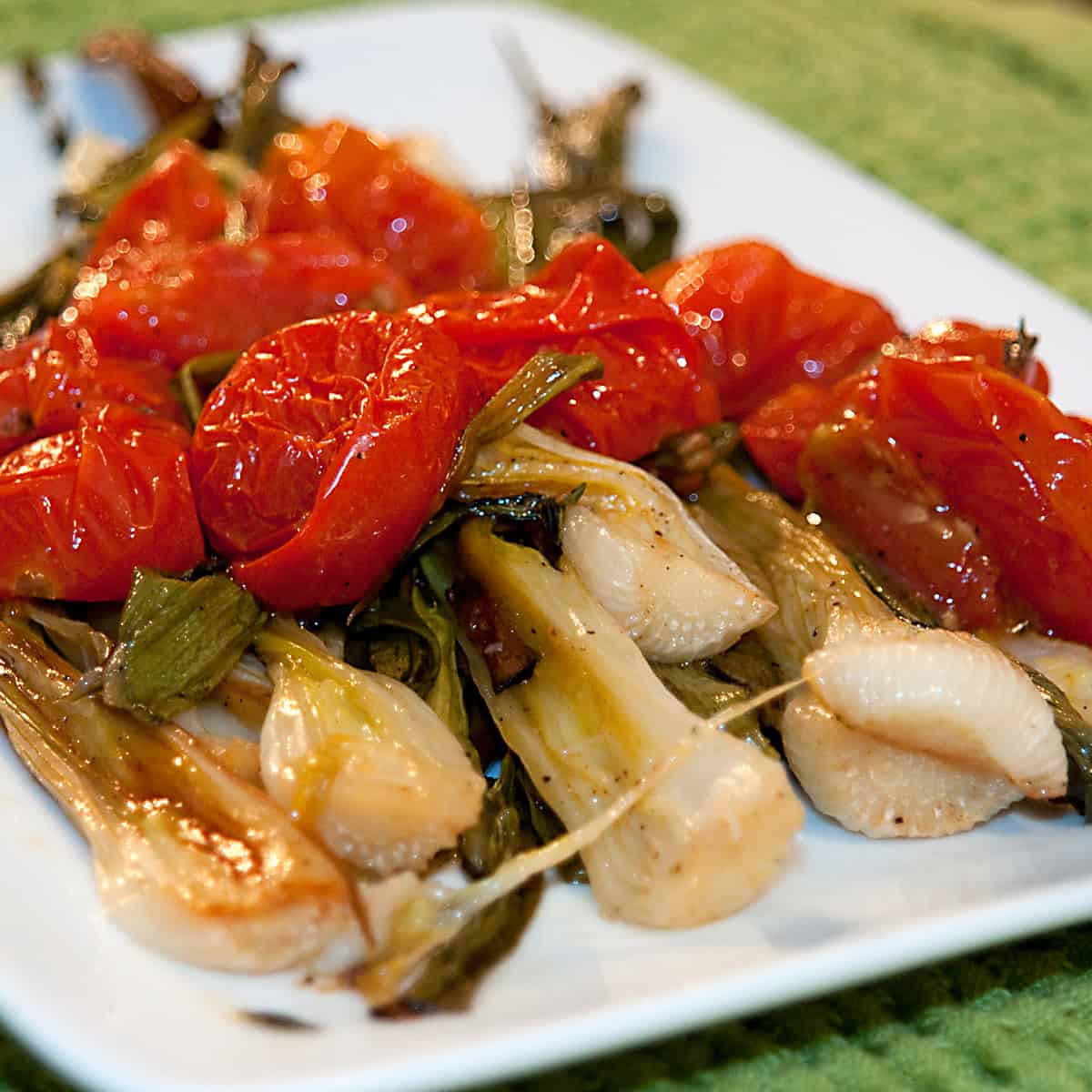 A white plate with roasted onions and tomatoes.
