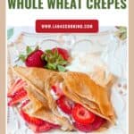 Whole wheat crepes filled with strawberries and cream, served with extra strawberries and whipped cream on a plate.