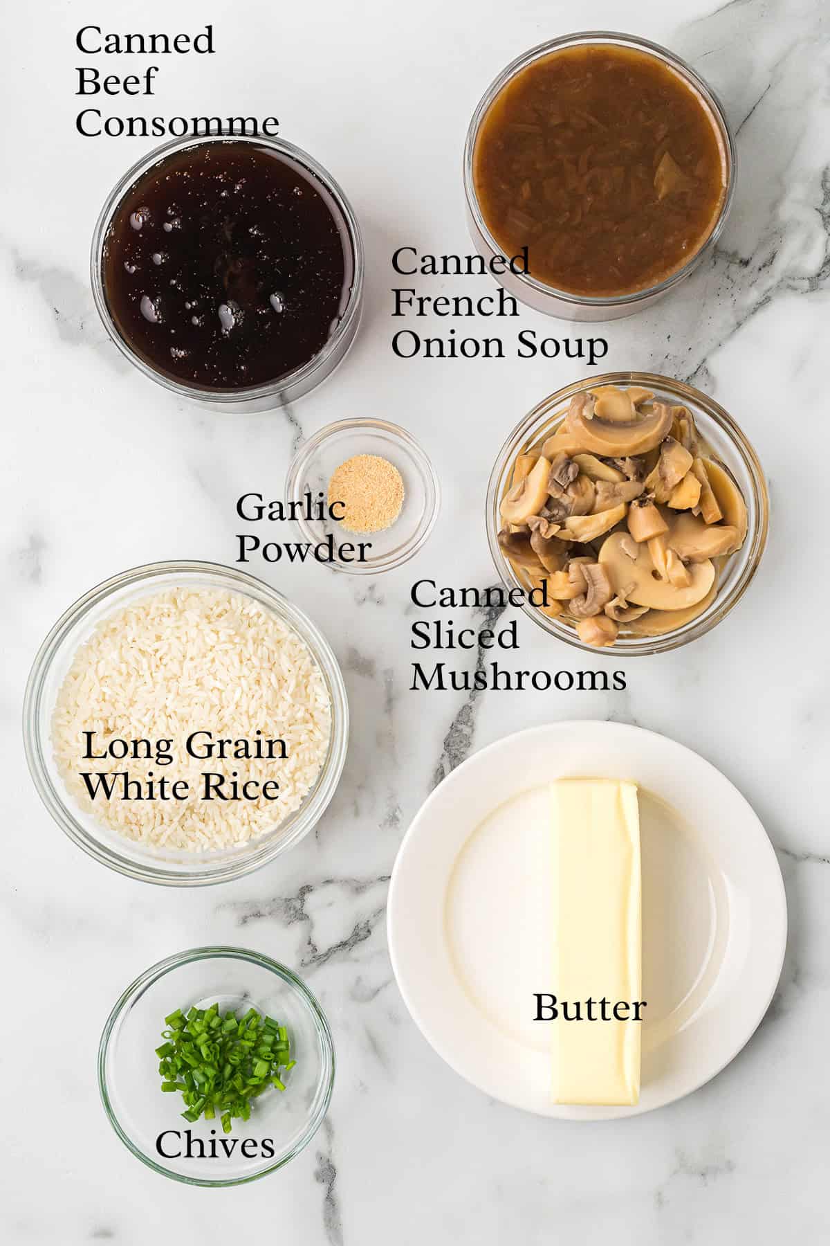 Ingredients including rice, canned soups, mushrooms, butter, garlic powder, and chives on a marble surface.