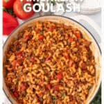 A pot of American goulash with macaroni, ground beef, and tomatoes, surrounded by fresh tomatoes and parsley.