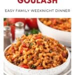 Bowl of American goulash with macaroni, ground meat, tomatoes, and herbs on a table.