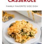 A serving of cheesy broccoli rice casserole on a white plate, with a casserole dish in the background.