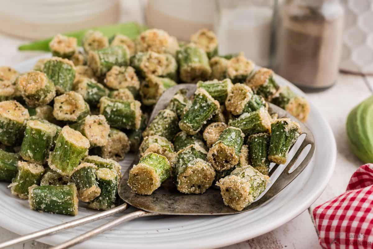 Fried okra on a white plate with a portion in a metal slotted scoop.