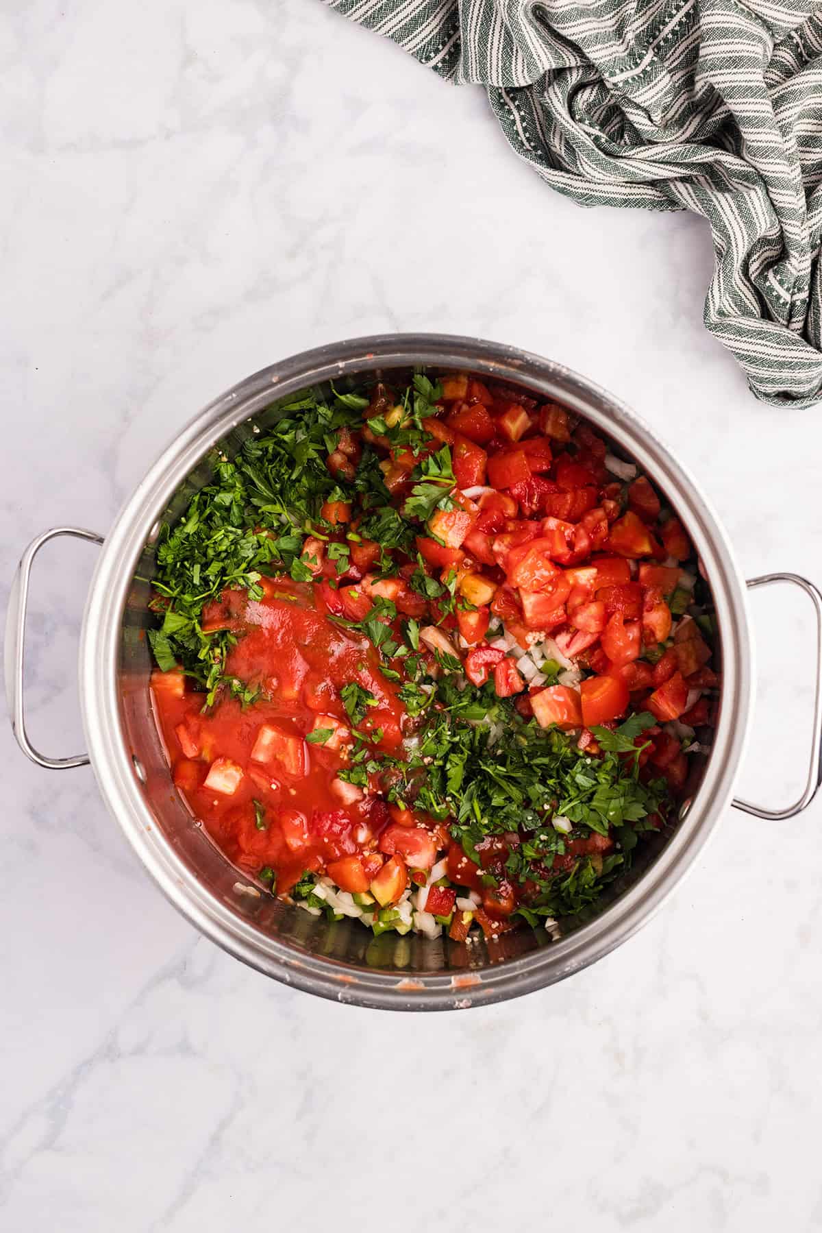 Chopped tomatoes, onion, garlic, and peppers in a saucepan.