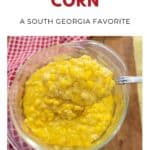 A bowl of creamy yellow creamed corn with a spoonful lifted, on a wooden table with a red-check cloth.