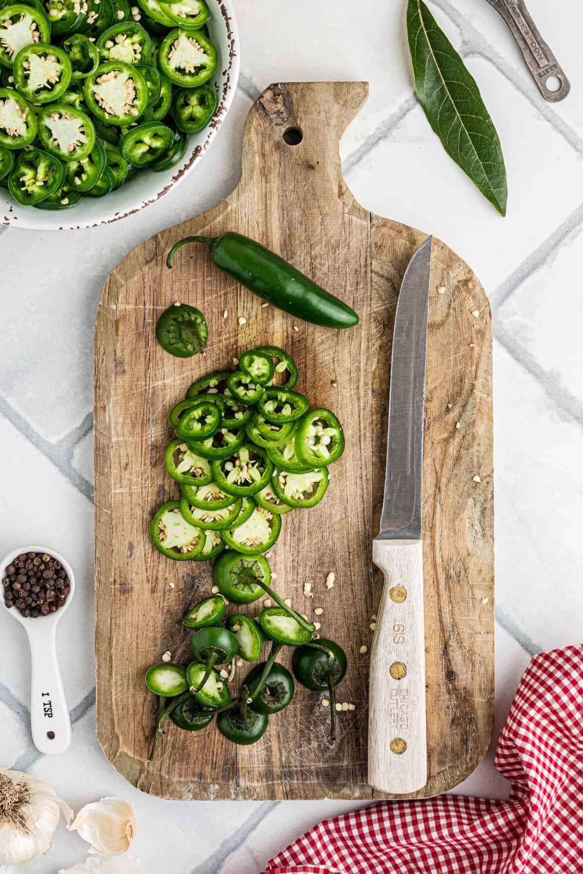 Jalapenos sliced on a cutting board on a tile background.