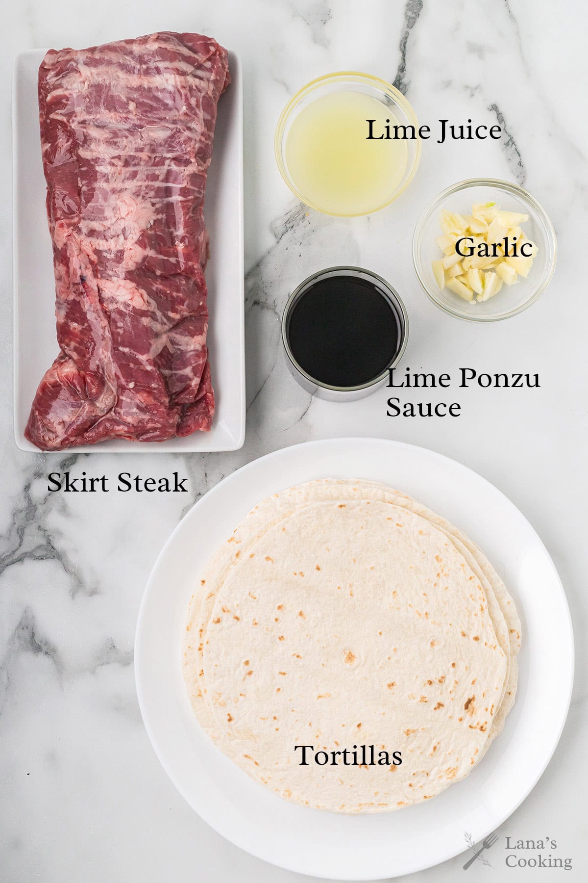 Raw skirt steak, lime juice, garlic, lime ponzu sauce, and tortillas arranged on a marble surface.