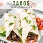 Two carne asada tacos with cilantro on a plate, served with lime and salsa, with toppings in the background.