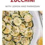 Sliced pan-fried zucchini topped with shredded parmesan and lemon on a white plate with a fork.