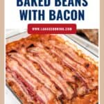 A baking dish filled with baked beans topped with several strips of cooked bacon.