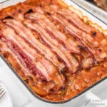Baked beans in a dish topped with several strips of cooked bacon.