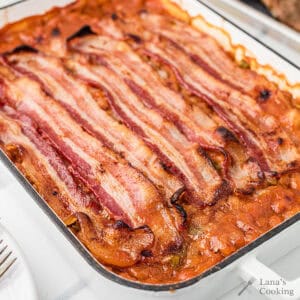 Baked beans in a dish topped with several strips of cooked bacon.