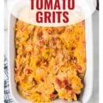 Baked cheesy tomato grits in a white dish, topped with melted cheese, with a spoon on the side.