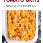 Baked cheesy tomato grits in a white dish, topped with melted cheese, next to a spoon and towel.