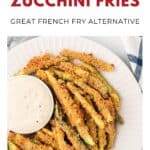 Plate of breaded zucchini fries with a cup of dipping sauce, next to a blue striped napkin.