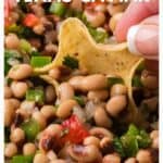 A hand dips a tortilla chip into a colorful Texas caviar dip with peppers and herbs.