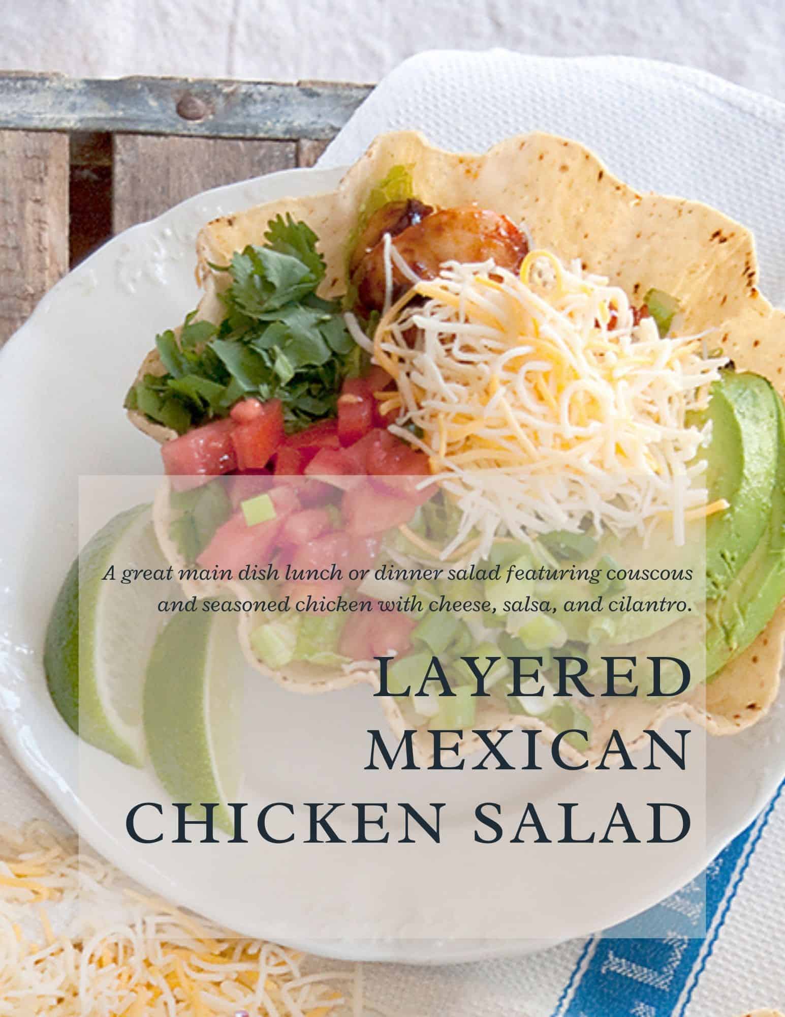 A tortilla bowl with layered Mexican chicken salad, including shredded cheese, diced tomatoes, avocado slices, couscous, cilantro, and seasoned chicken, served on a white plate with lime wedges. Text overlay describes the dish.