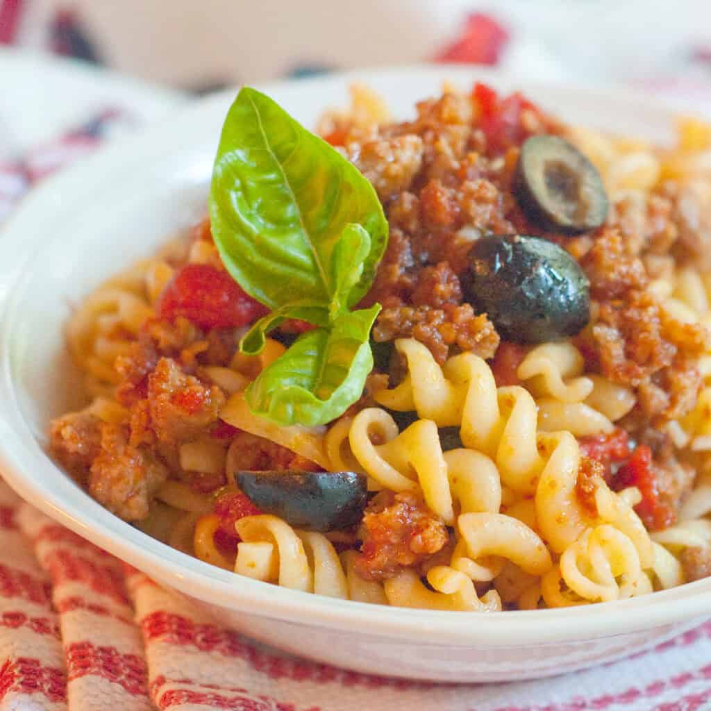 A serving of Italian sausage with rotini in a white bowl.