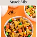 Bowl of Halloween snack mix with candy corn, pretzels, and cereal on an orange background.