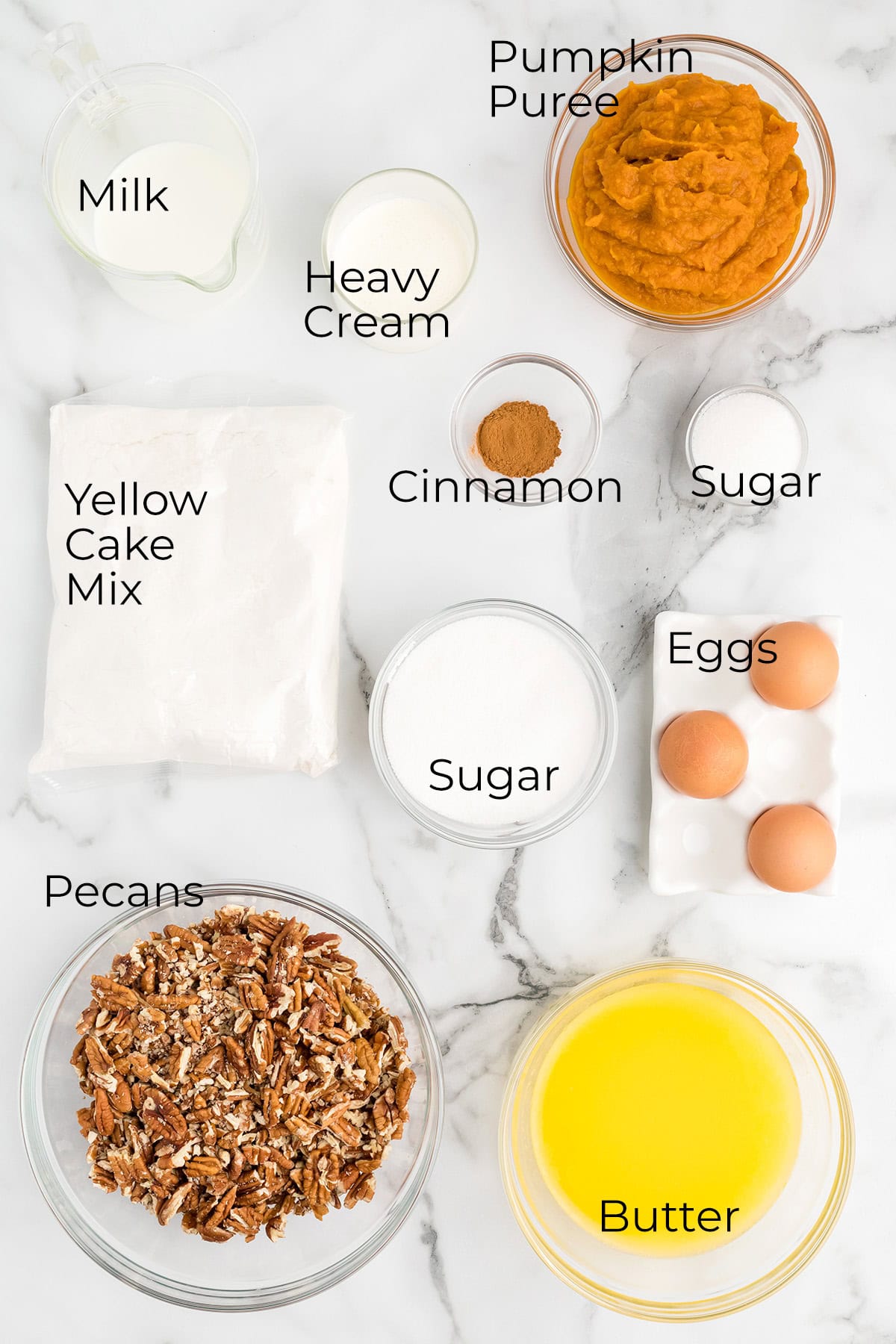 Labeled ingredients for pumpkin dessert: milk, cream, pumpkin puree, cake mix, cinnamon, sugar, eggs, pecans, butter.