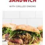 Steak sandwich with grilled onions, arugula, and sauce on a ciabatta roll, served on a white plate.