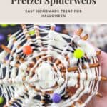 Hand holding a white chocolate pretzel spiderweb with candy spiders on a festive Halloween background.