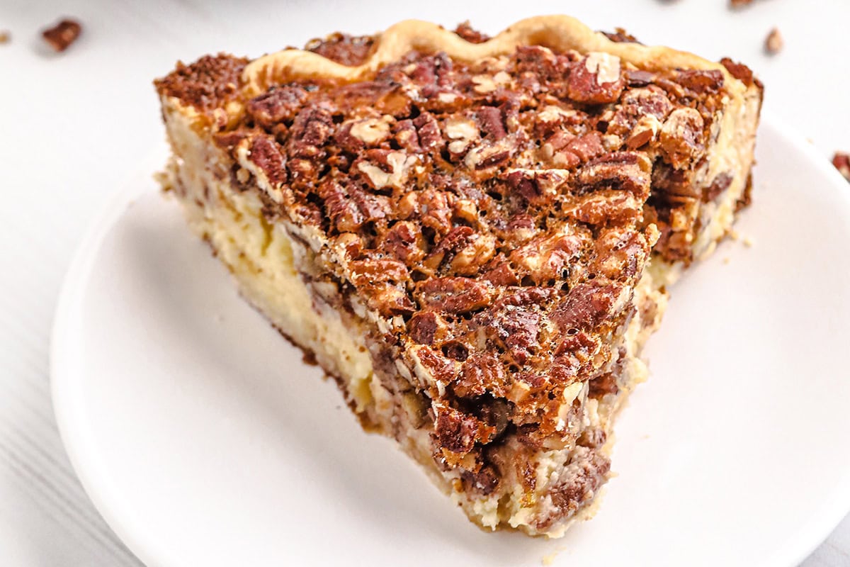 A slice of pecan cheesecake pie with a golden crust on a white plate.