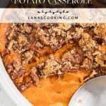 A sweet potato casserole topped with pecans and brown sugar in a white dish with a serving spoon.