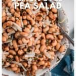 A bowl of black eyed pea salad topped with sliced onions, on a blue and white cloth.