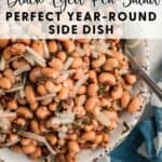 A bowl of black-eyed pea salad with onions and herbs, placed on a table next to a blue napkin and a spoon.