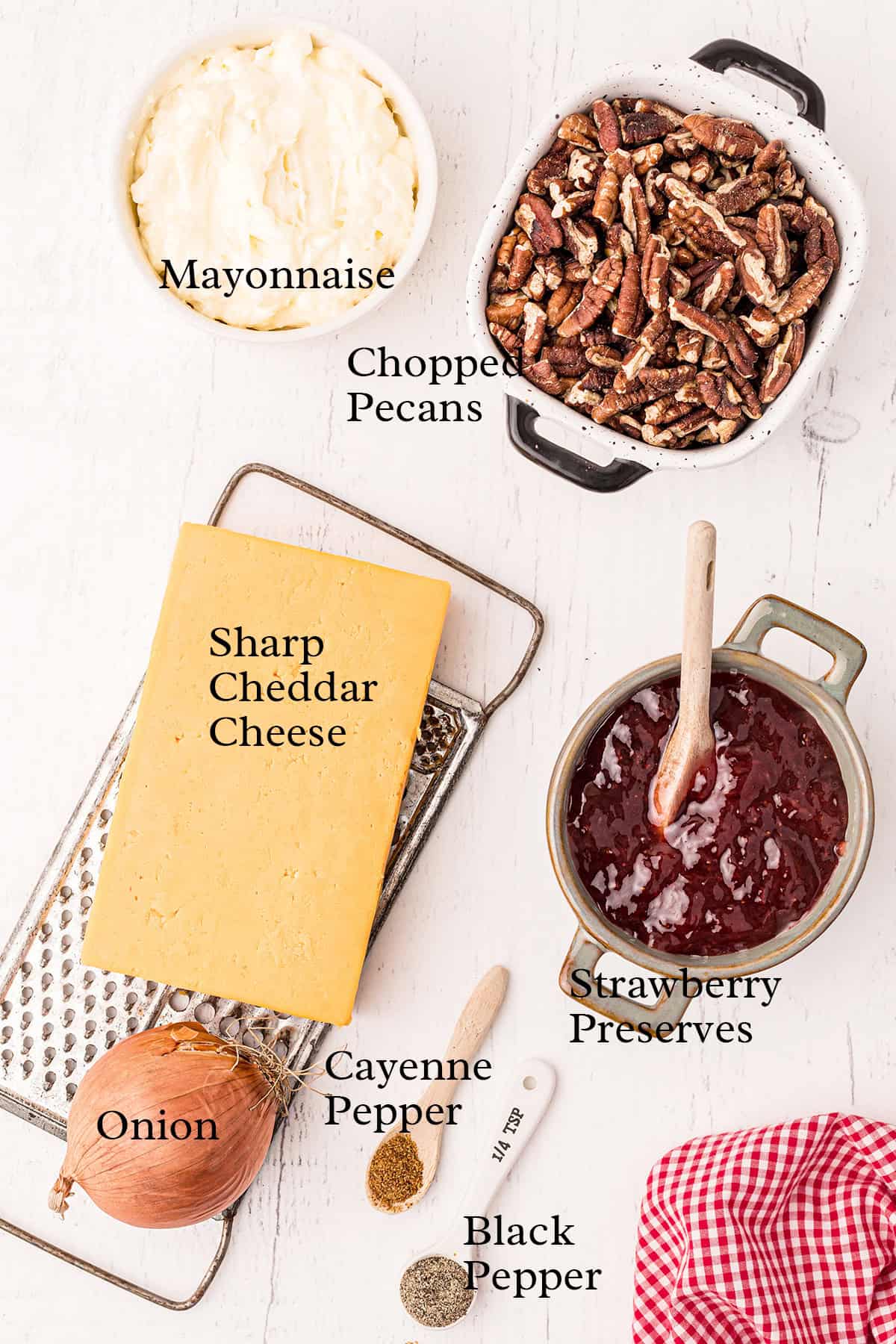 Ingredients on a white table: mayo, cheddar cheese, pecans, strawberry preserves, onion, cayenne, and black pepper.
