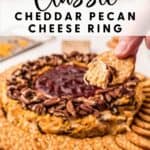 A hand dips a cracker into a cheddar pecan cheese ring with jam center, surrounded by more crackers.