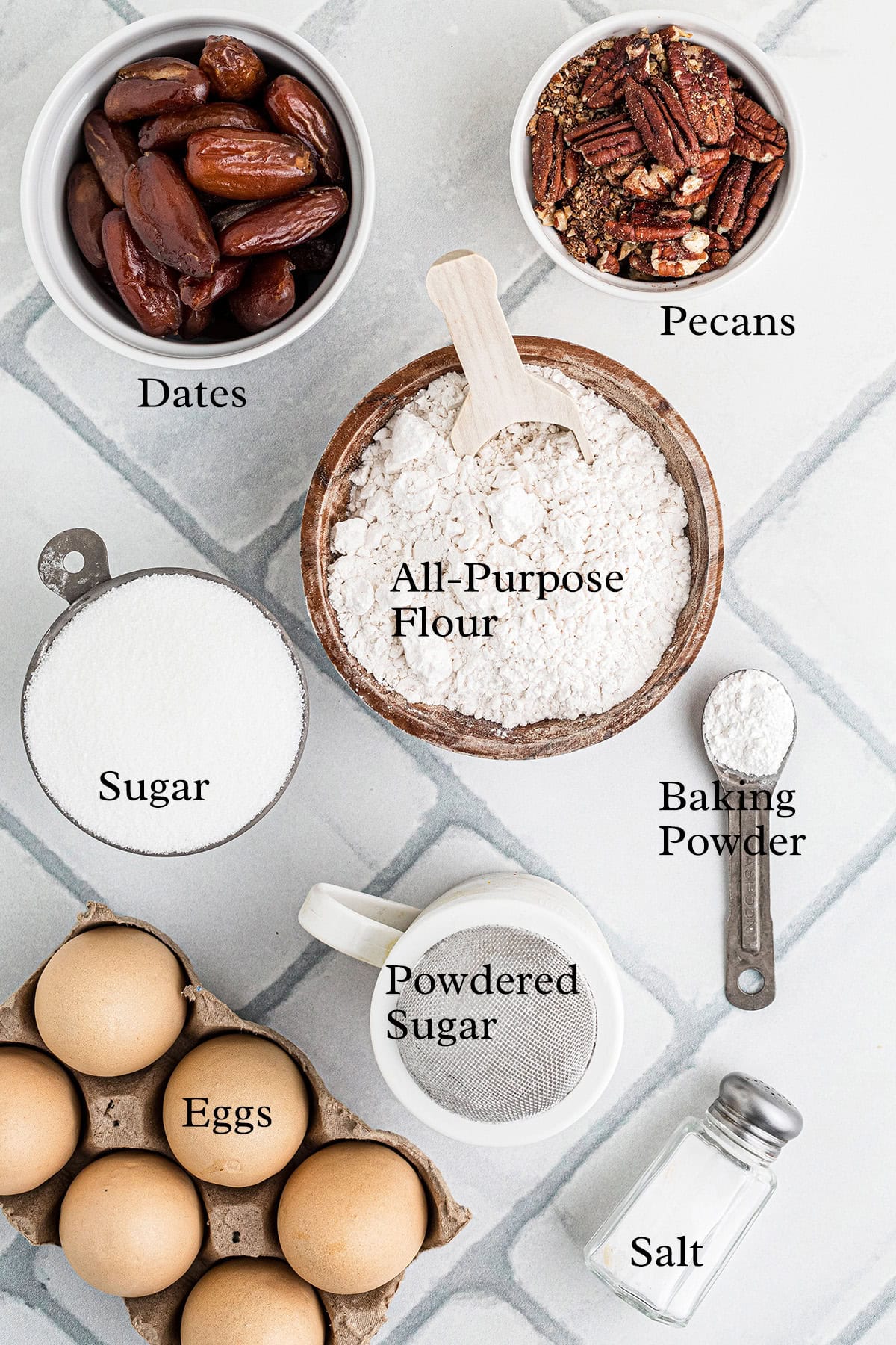 Top view of baking ingredients: dates, pecans, flour, sugar, baking powder, eggs, powdered sugar, and salt.