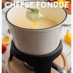A white pot of cheese fondue with broccoli dipped on a fork, surrounded by colorful vegetables.