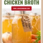 Jars of homemade chicken broth with tags, surrounded by an onion, carrots, and peppercorns.
