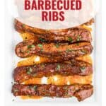 Six glazed, barbecued ribs on a white platter, garnished with herbs. Text: Slow Cooker Barbecued Ribs.