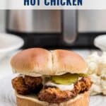 A Nashville hot chicken sandwich with pickles and sauce on a plate, air fryer in the background.