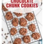 A cooling rack with double chocolate chunk cookies, some cookies and chocolate chunks scattered on a white surface.